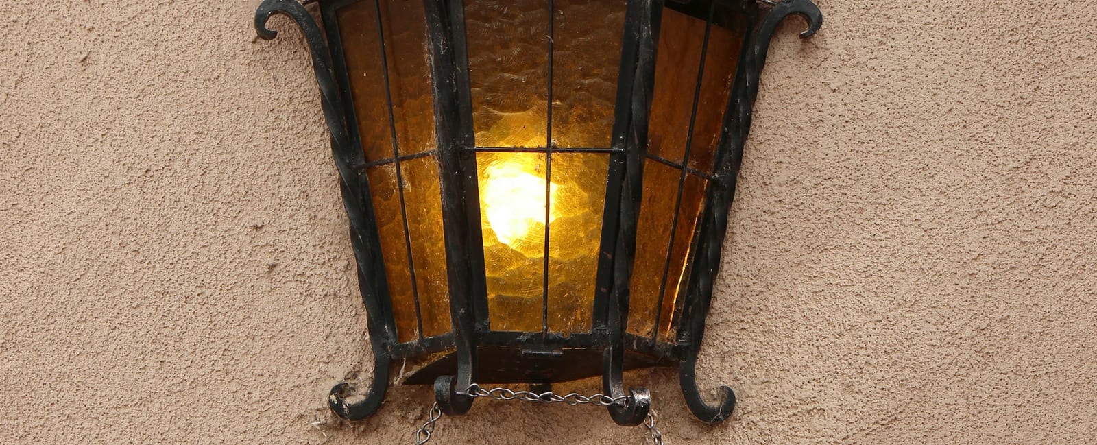 A wrought iron lamp on a stucco wall above a shop door.