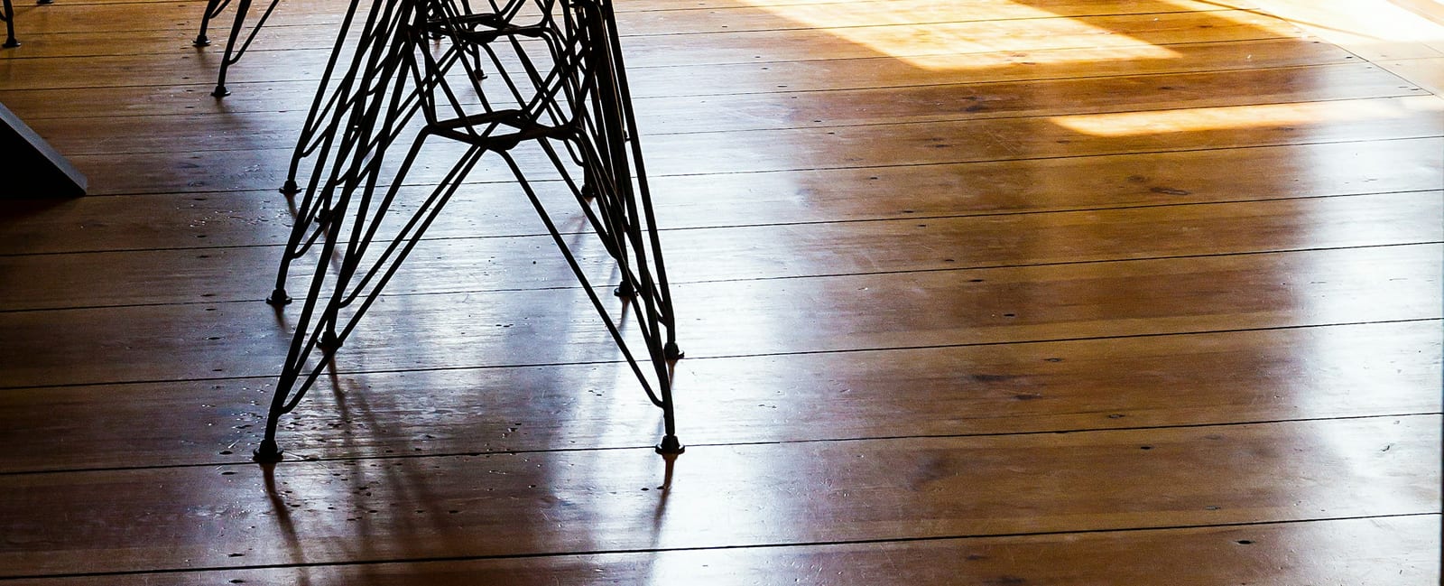 Wire chair legs on a sunlit wooden floor.
