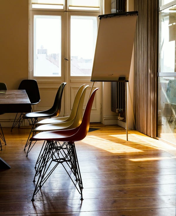 Empty chairs facing a flip chart in a sunlit room.